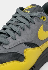 Gray suede sneaker with mesh accents, yellow midsole, and logo. Features gray laces and a cushioned collar. Curved design details.