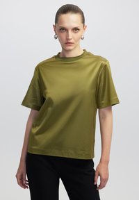 Olijfgroene top met korte mouwen en een ronde halslijn, gemaakt van gladde, glanzende stof. Heeft een ontspannen pasvorm en een minimalistisch ontwerp.