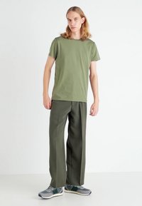 Oliwkowa bawełniana koszulka z krótkim rękawem, zestawiona z luźnymi oliwkowymi spodniami i szarymi butami sportowymi z zielonymi akcentami.