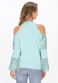 Világoskék, kötött pulóver, nyitott vállakkal, hosszú ujjaival, ezüst fröccsöntési díszekkel és magas nyakkivágással. Puha tapintású.