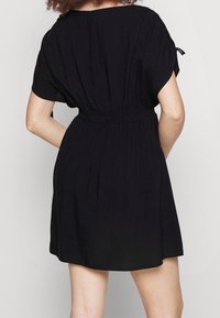 Robe noire courte avec une coupe décontractée, une taille élastique et des manches froncées. Tissu lisse avec un ourlet fluide.