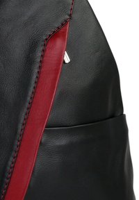 Sac en cuir noir avec une rayure rouge et des coutures contrastantes. Comprend un détail métallique près de la couture pour un intérêt supplémentaire.