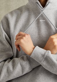 Sudadera de algodón gris con un alto cuello, cordones cruzados y puños acanalados. El nombre de la marca "SANDRO" está sutilmente bordado en la parte delantera.