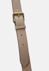 Béžový kožený opasek s zakřiveným koncem, vybavený zlatým kovovým příslušenstvím a viditelným švem, umístěný s nastavitelnými dírami.