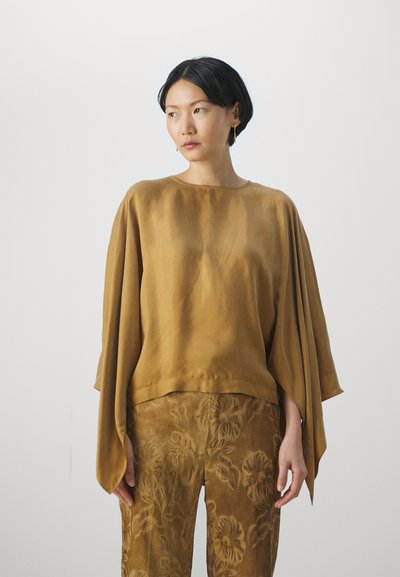 Camicia in satin bronzo con maniche ampie, abbinata a pantaloni beige con texture floreale. Finitura liscia e design dalla vestibilità rilassata. Stile minimalista.