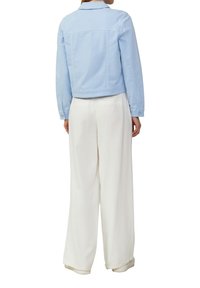 Veste en denim bleu clair à manches longues, au design cropped, avec des accents cousus et un col, portée sur un pantalon large blanc.