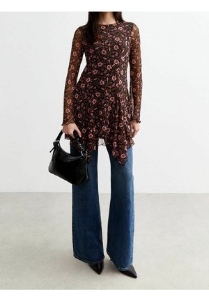 Kvinde iført en langærmet, gennemsigtig blomstret tunika, brede blå jeans, sorte spidse sko og holder en sort håndtaske.
