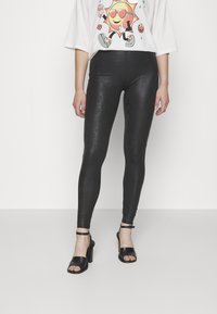 Leggings imprimés serpent noir avec une finition brillante, style ajusté, accompagnés de sandales noires à talon bloc et bride de cheville.