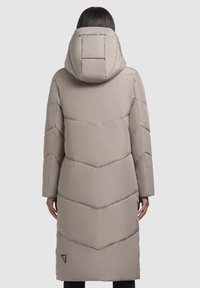 Garš bež pufīgais mētelis ar kapuci, ar čevrona šuvēm un mazu logotipu apakšējā kreisajā stūrī, ar gludu, matētu tekstūru.