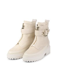 Bottines en daim beige avec semelles en caoutchouc blanc épaisses, dotées d'une fermeture éclair latérale, d'une sangle décorative avec quincaillerie dorée et d'une étiquette logo.