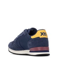 Zapatillas de ante azul marino con acentos en amarillo y marrón, que cuentan con un talón texturizado, un cuello acolchado y una suela a rayas para un detalle adicional.