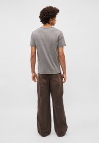 Camiseta de algodón gris con mangas cortas, combinada con pantalones marrones de pierna ancha que cuentan con bolsillos y un acabado texturizado.