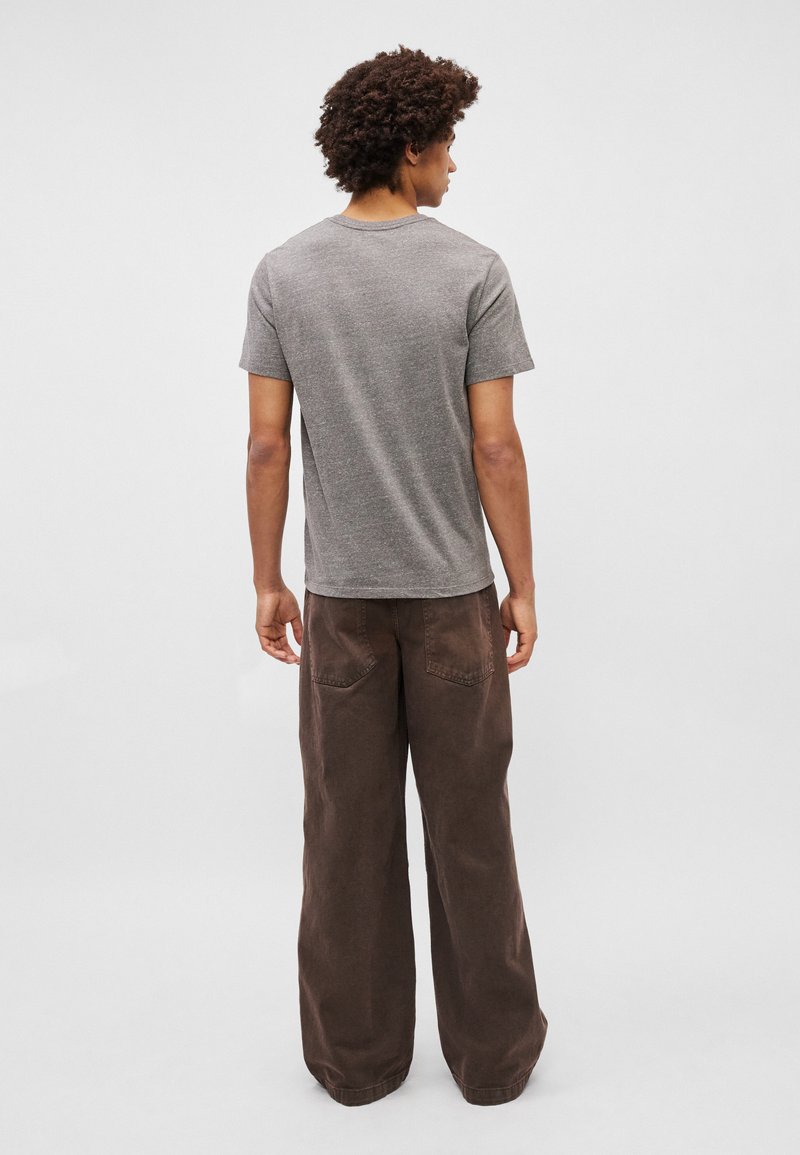 Szary bawełniany t-shirt z krótkim rękawem, zestawiony z brązowymi spodniami o szerokich nogawkach, które mają kieszenie i teksturowane wykończenie.