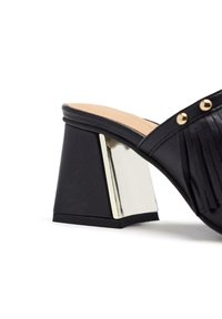 Mules à talons en cuir noir avec un bloc de talon accentué de métal, des détails frangés et des ornements en studs dorés sur le dessus.