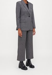 Grå skräddarsydd blazer med en knapp, två framfickor och matchande capribyxor; kombinerad med svarta klumpiga stövlar.