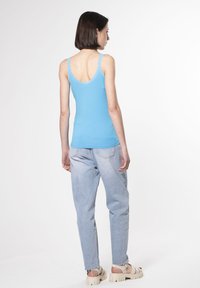 Top sin mangas azul con encaje en el borde, combinado con jeans de tiro alto de un azul claro. El conjunto presenta un corte relajado y un diseño simple.