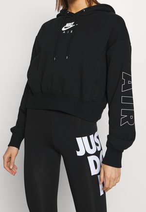 Černá zkrácená mikina s kapucí a šňůrkami, s bílým logem Nike a textem "AIR" na rukávu. Spárováno s černými legínami, které nesou text "JUST DO IT" v bílé barvě.