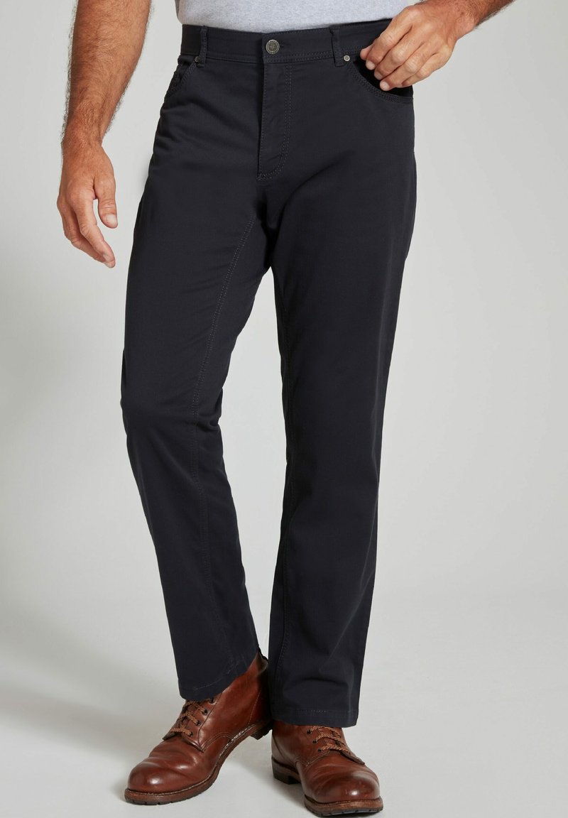 Donkerblauwe katoenen broek met een slank model, voorzien van een ritssluiting, knoopsluiting, zijzakken en subtiele stikseldetails. Bruine leren schoenen.