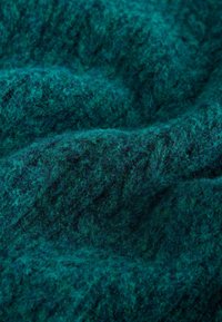 Tume teali tekstuuriga kangas, millel on karvane ja pehme välimus, näidates kihiliselt paigutatud erinevate tooni ja kiudude segu.