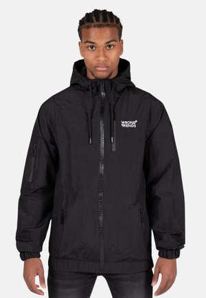 Schwarze Kapuzenjacke aus leichtem Material. Merkmale sind elastische Bündchen, ein Frontreißverschluss mit Logodetail und seitliche Taschen. Auffälliges Branding auf der Brust.