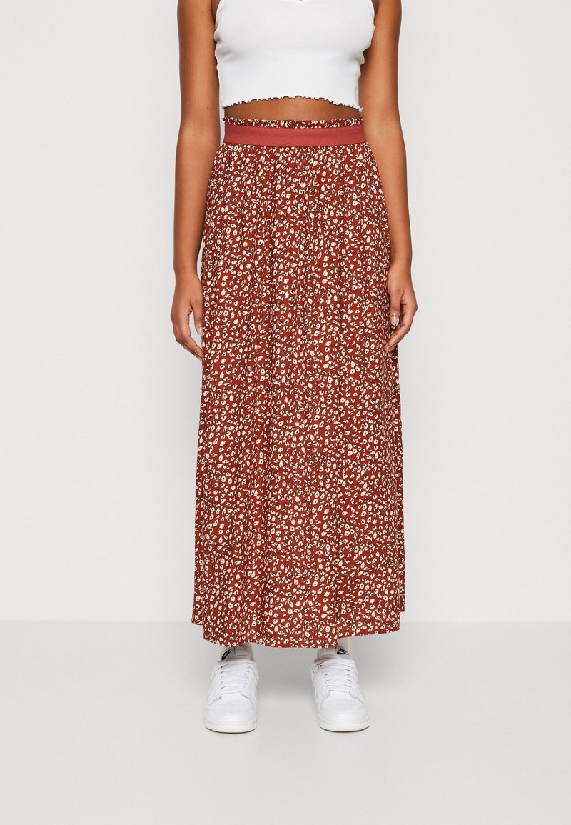 Falda larga floral roja con cintura elástica, que presenta un estampado blanco y un diseño fluido. Combinada con zapatillas blancas.