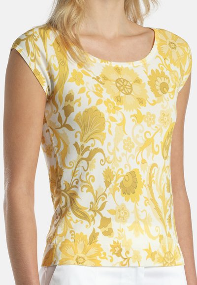Weißes kurzärmliges Oberteil mit gelben Blumen- und Blattmustern, in figurbetontem Stil, getragen von einer Person mit heller Haut und blondem Haar.
