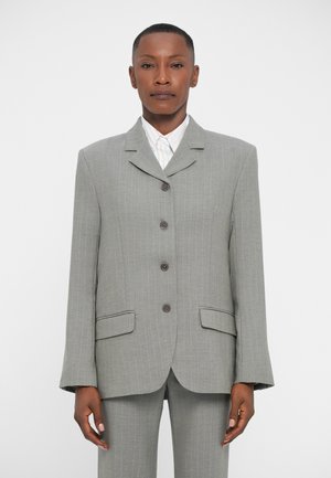 Harmaa pinstripe-puku takki, jossa on viistekulmainen kaulus, viisi nappia ja kaksi etutaskua. Myös housut näkyvät.
