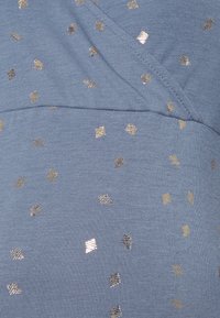 Tecido azul com uma textura suave, apresentando formas de diamante metálicas douradas e prateadas dispersas em um padrão repetido.