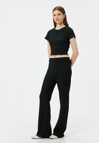 Zwart, gestructureerd tweedelig outfit met een kortoling cropped top en uitlopende broek, beide met een subtiel, kreukelig ontwerp en een elastische tailleband.
