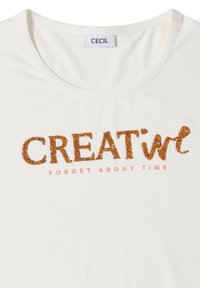 Chemise blanche à encolure ronde avec les mots « CREATIVE » en orange pailleté et « FORGET ABOUT TIME » en plus petites lettres couleur pêche en dessous.