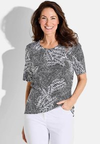 Schwarzes und weißes T-Shirt mit Blattmuster, weicher Stoff, runder Ausschnitt, lockere Passform, kombiniert mit weißen Hosen.