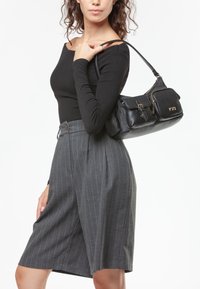 Top a maniche lunghe nera abbinato a pantaloni corti grigi a righe a vita alta. Il modello porta una grande borsa in pelle nera con dettagli dorati.