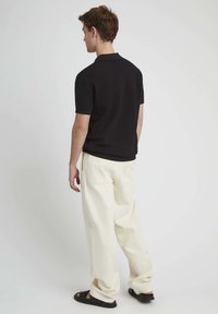 Polo shirt noir texturé associé à un pantalon ample couleur crème et des sandales noires. L'ensemble présente un design décontracté et relax.