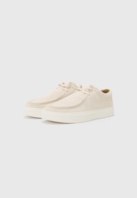 Sneaker in suede beige con punta arrotondata, dettagli cuciti e chiusura con lacci. Suola in gomma con un leggero rialzo.