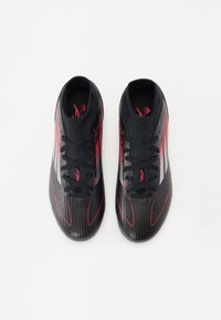 Black soccer cleats with red accents, featuring a ribbed texture, lace-up design, and streamlined shape. Notable silver branding on the sides.