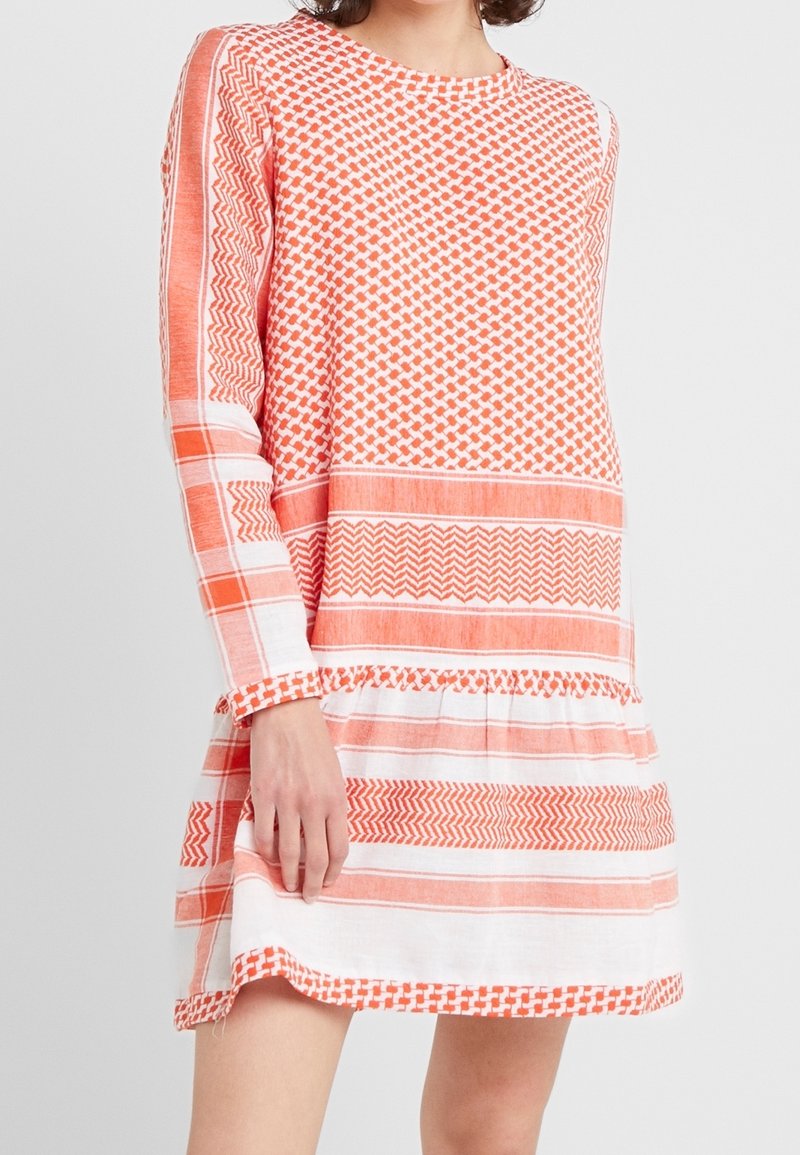 Vestido de patrones naranjas y blancos con mangas largas, que presenta diseños geométricos y rayas horizontales. Hecho de una tela ligera.