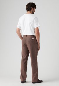Bruine katoenen broeken met een rechte snit, voorzien van een achterzak met knoopsluiting en een klein logo label. Draag dit met een witte shirt met korte mouwen.