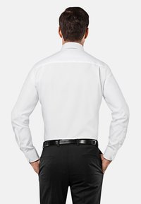 Witte dress shirt met lange mouwen, voorzien van een klassieke kraag en knoopaccenten, gecombineerd met zwarte broek en een zwarte riem.