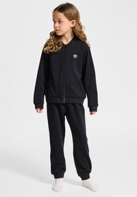 Svart zip-up sweatshirt med framficka, matchad med svarta joggers. Tyget är mjukt, med ribbade mudd och en liten logotyp på bröstet.