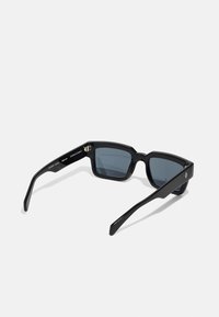 Black square sunglasses with dark lenses, thick frames, and a subtle logo on the temples. Smooth texture and angular design.