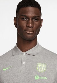 Grau Poloshirt mit poloartigen Kragen, featuring neongrünes Nike-Logo, Barcelona-Wappen und Spotify-Logo. Aus Baumwollmischung und mit strukturiertem Finish.