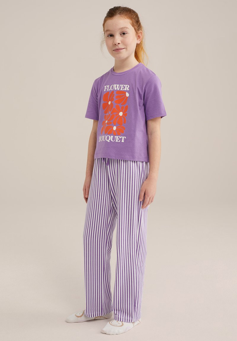 Violeta T-krekls ar "Ziedu pušķa" grafiku un sarkaniem ziediem; apvienots ar violetiem un baltajiem svītrainajiem pidžamu biksēm. Kokvilnas materiāls, brīvas piegriezuma.