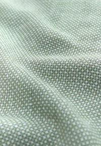 Textured fabric in light green, featuring a woven pattern of small squares. The material appears soft and slightly crumpled.