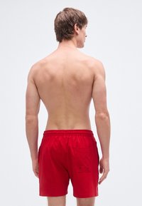 Κόκκινα μαγιό σορτς με ελαστική μέση και τσέπη στο πίσω μέρος. Το υλικό φαίνεται λείο, το ύφασμα ελαφρύ, χωρίς ορατά σχέδια ή διακοσμητικά στοιχεία.