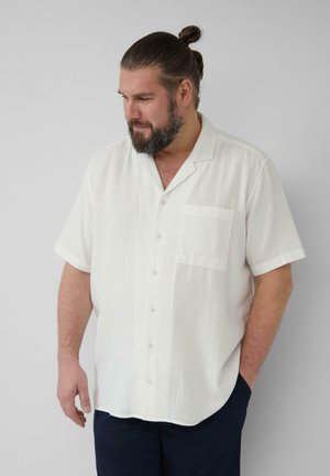 Chemise à manches courtes, à boutons, en tissu blanc léger et texturé, avec une poche poitrine unique et un col ouvert.