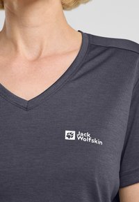 Donkergrijze v-hals t-shirt gemaakt van zacht materiaal met een witte "Jack Wolfskin" logo en pootafbeelding op de linkerkant van de borst.