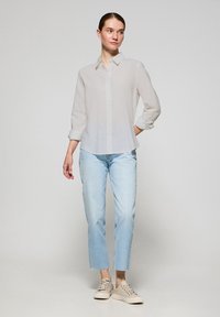 Lekka, przezroczysta biała koszula z długimi rękawami. W połączeniu z jasnoniebieskimi, skróconymi dżinsami i beżowymi sneakersami. Prosty design, swobodny fason.