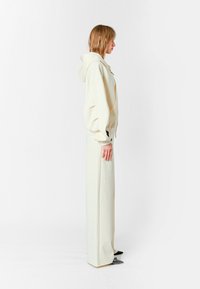 Sudadera oversized color crema con capucha, combinada con pantalones de pierna ancha en el mismo tono. Tejido suave, diseño minimalista y detalle de cremallera lateral.