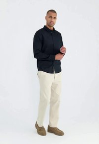 Chemise à manches longues bleu foncé avec fermeture à boutons, associée à un pantalon beige clair et des mocassins marron. Un design simple et classique.