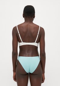 Sutien alb cu bretele ajustabile și închidere tip clips. Chilot deschis la culoare, cu o bandă elastică cu brand. Material neted cu un design ajustat.